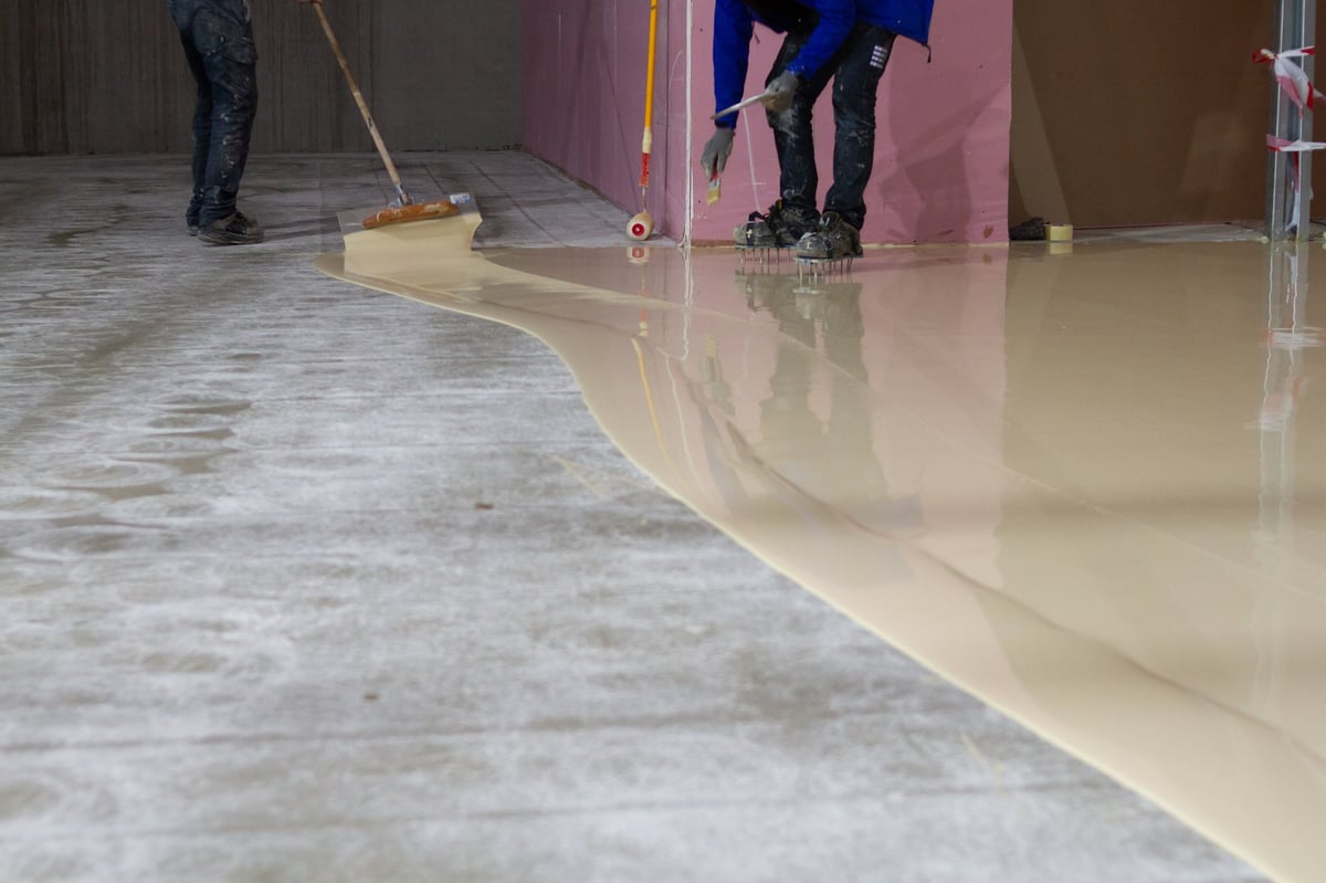 A skilled worker carefully applying durable epoxy resin coating to a concrete floor, demonstrating the finishing techniques used for garage and concrete coatings