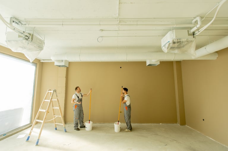 Two painters focused on painting a wall beige in a well-lit room