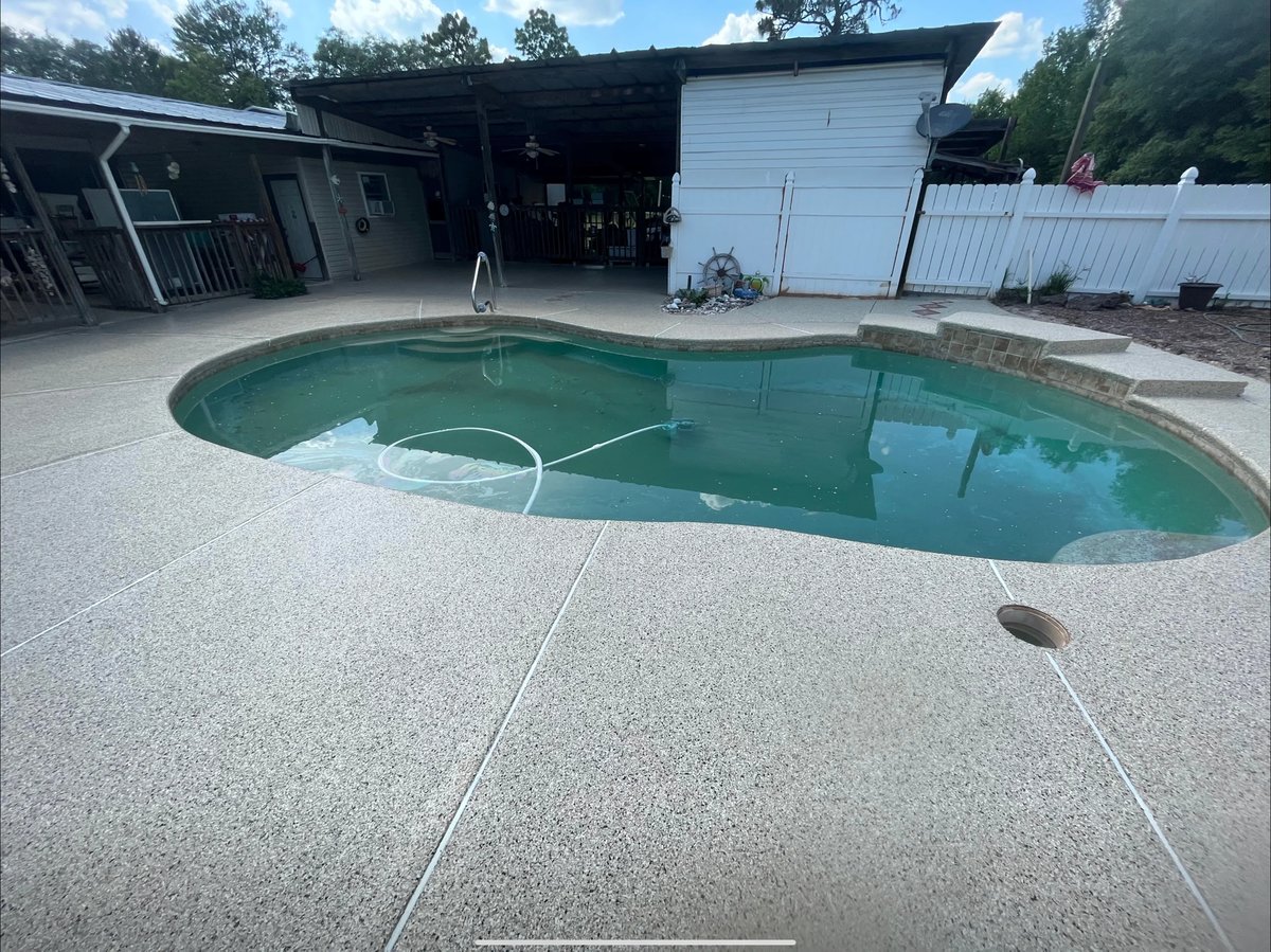Backyard residential pool with turquoise water and concrete deck surrounded by metal storage sheds and trees