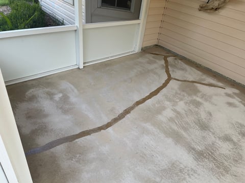Concrete patio floor with brown sealing lines creating curved patterns, white door and window visible in background