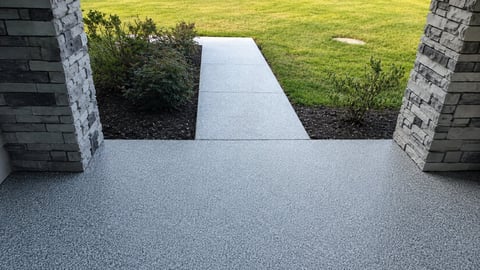 Modern home entrance with gray paved driveway, white concrete walkway, brick pillars, and manicured green lawn visible beyond