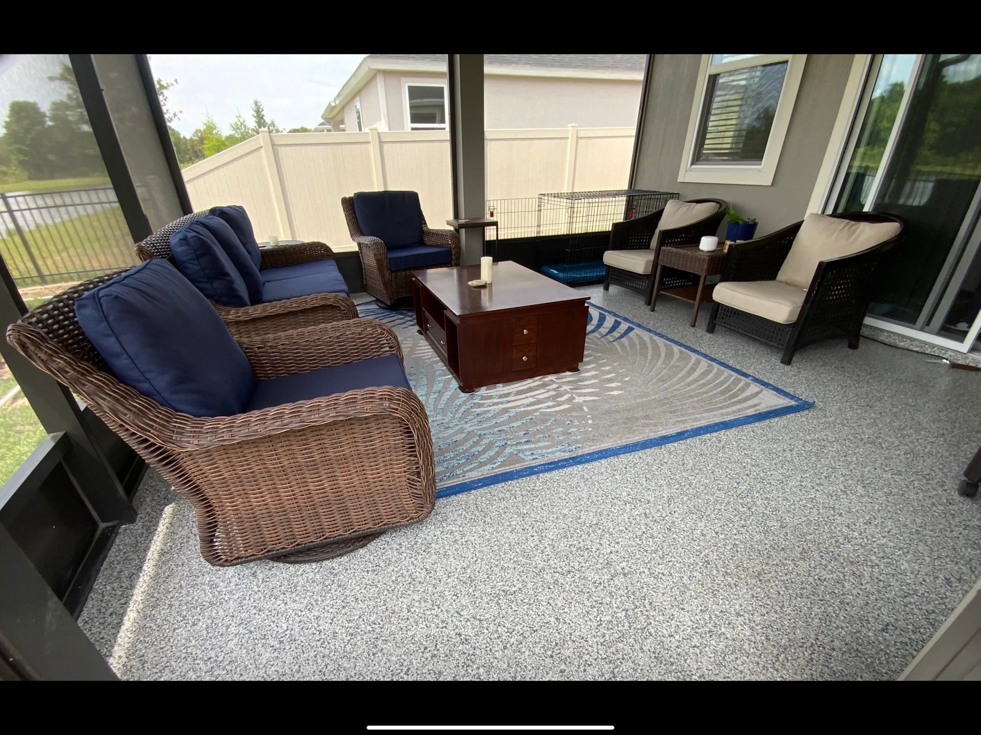 Covered patio with wicker furniture and navy cushions arranged around a wooden table on a blue and gray rug