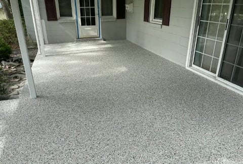 Finished concrete patio with speckled gray epoxy coating attached to a light gray house with windows and door
