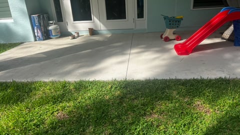 Red playground slide on concrete patio next to green lawn and house exterior