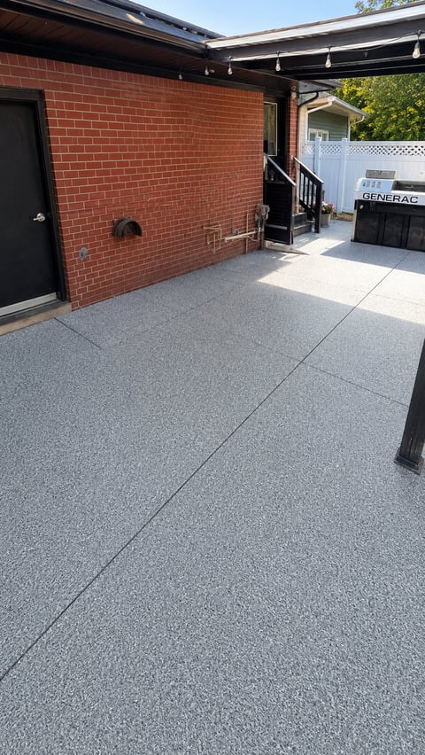 Modern patio with gray epoxy flooring, red brick building wall, black overhang, and generator visible in background