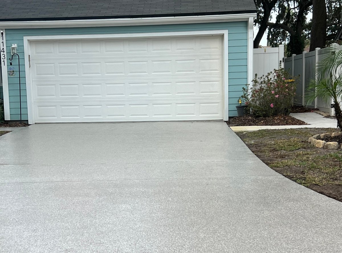Light blue house with white garage door and freshly paved concrete driveway