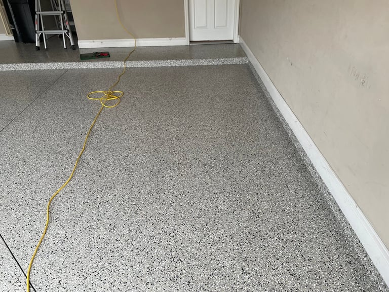 Empty garage interior with gray speckled epoxy floor, white trim, ladder, and yellow extension cord