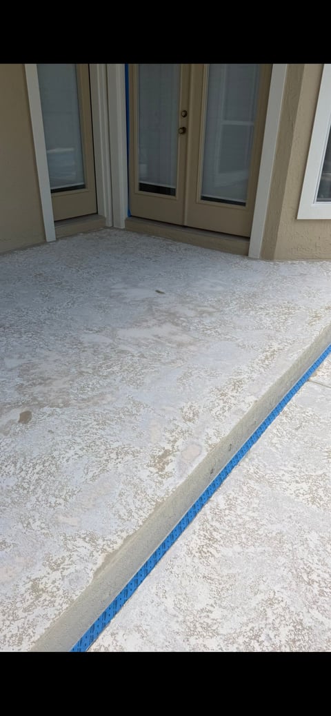 Concrete patio with blue tape line leading to glass sliding doors and windows