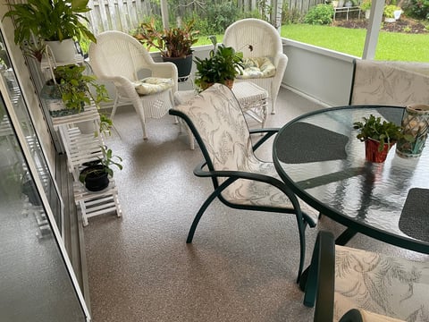 Covered porch with wicker chairs, potted plants, and two tables overlooking a green lawn and wooden pergola