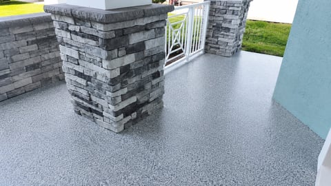 Stacked gray brick pavers on light gray concrete driveway with white fence gate and lawn visible