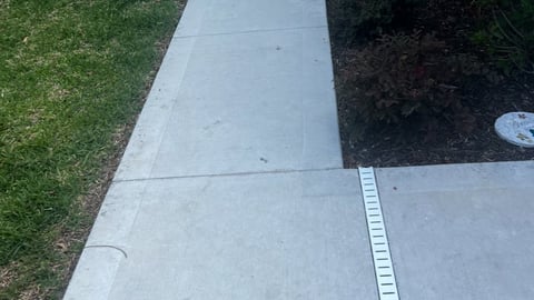 Concrete sidewalk with metal edge trim next to green lawn and dark mulch landscaping