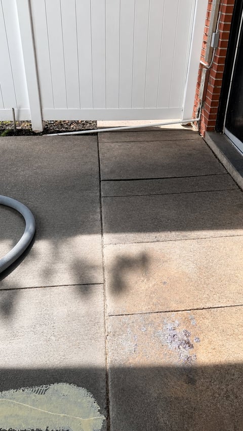 Concrete driveway with white garage door and red brick wall, showing age spots and shadow from overhead object