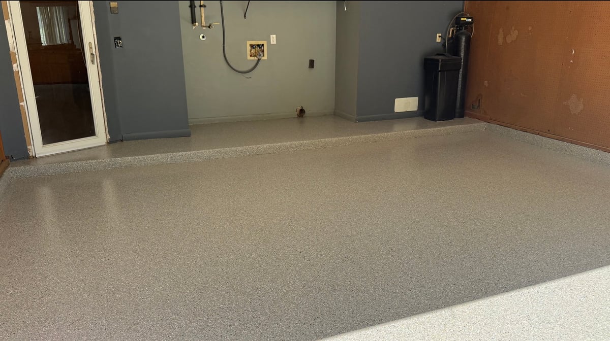 Empty garage interior with gray epoxy floor, blue wall, electrical outlets, and brown door visible