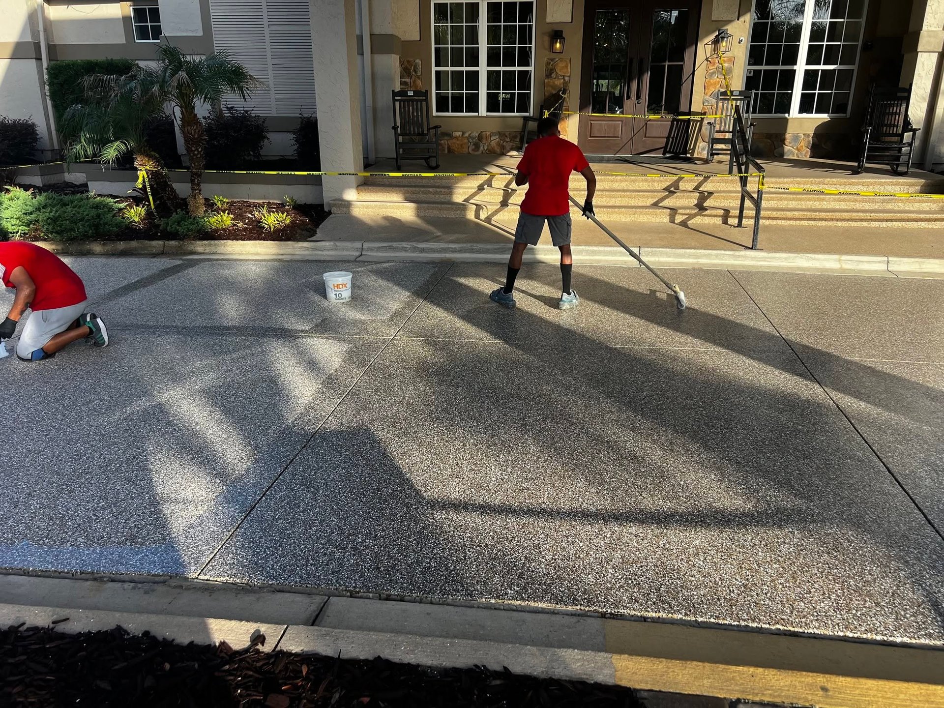 People cleaning and maintaining a large residential driveway with pressure washing equipment in bright daylight
