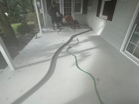 Garden hose on white concrete porch with person and equipment visible in background near house