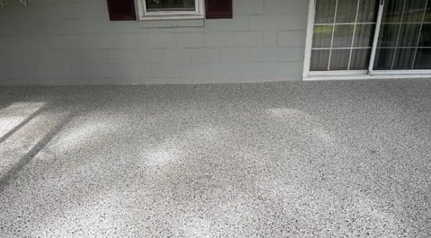 Epoxy-coated garage floor with speckled gray finish, white house wall and windows in background