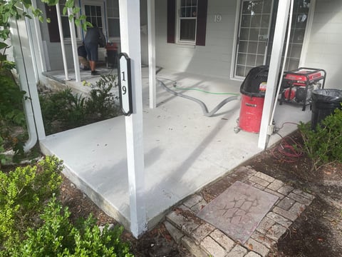 Newly poured concrete patio attached to white house with tools and red equipment on surface