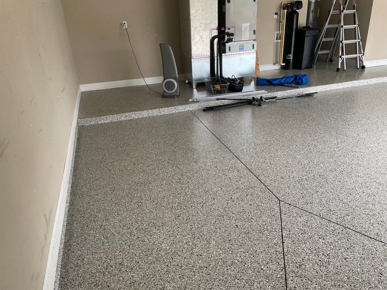Unfinished concrete garage floor with tools and equipment staged along the back wall during renovation