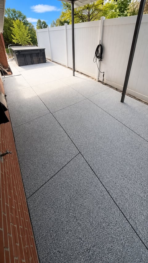 Modern backyard patio with gray stone pavers, white privacy fence, and utility connections on sunny day