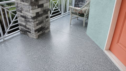 Modern covered porch with gray speckled concrete floor, brick column, white railings, and coral red door