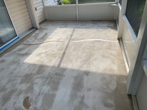 Empty concrete patio with control joints, enclosed by white walls and windows on a sunny day