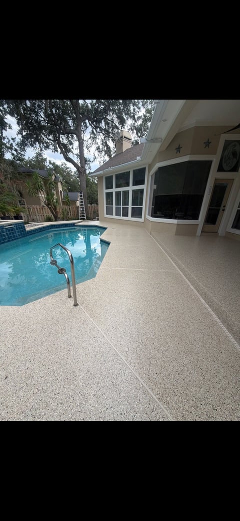 Backyard pool and patio area with clear blue water, concrete deck, and cream-colored pool house with large windows