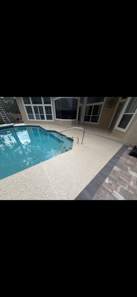 Indoor residential swimming pool with curved edges, beige concrete deck, and adjoining home with large windows and clock