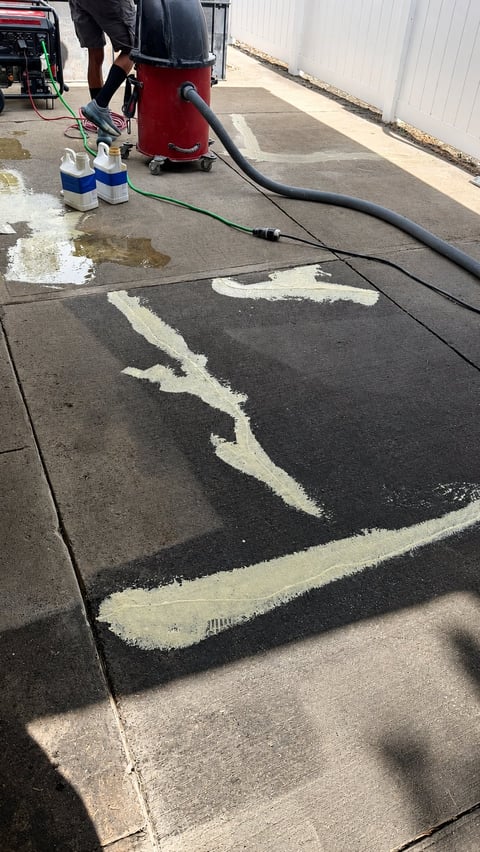 Concrete surface being pressure washed with white chalk markings, red cleaning equipment, and hoses visible